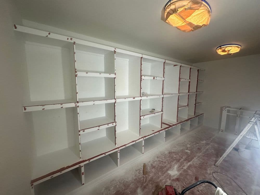 Custom white shelving unit under construction in a room with a dusted floor and ceiling lights.