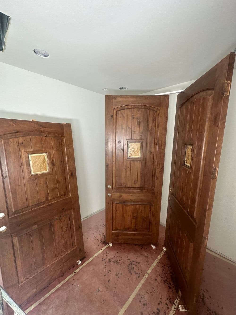 Three wooden doors with glass panels leaning against a wall in an unfinished room.