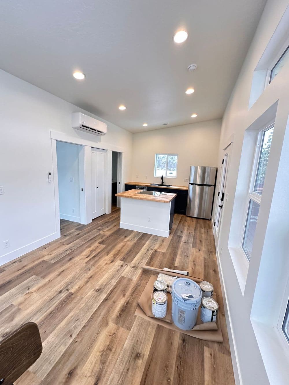 Modern kitchen interior with wooden floors, island, stainless steel fridge, and paint cans.