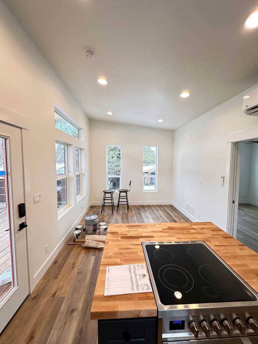 Modern kitchen with wooden flooring, countertop stove, and dining area with two chairs.