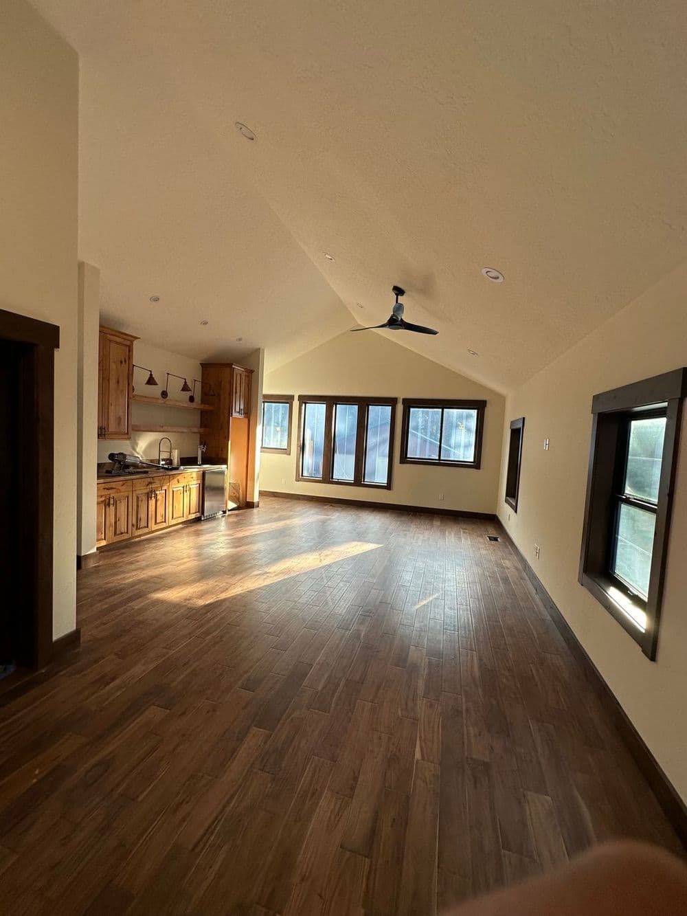 Spacious, sunlit room with wooden floors, kitchen area, and large windows.