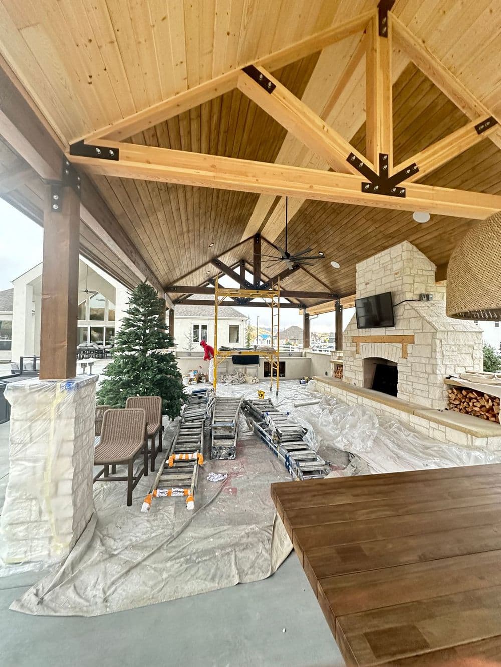 Outdoor entertainment area with construction underway, featuring a stone fireplace and wooden beams.