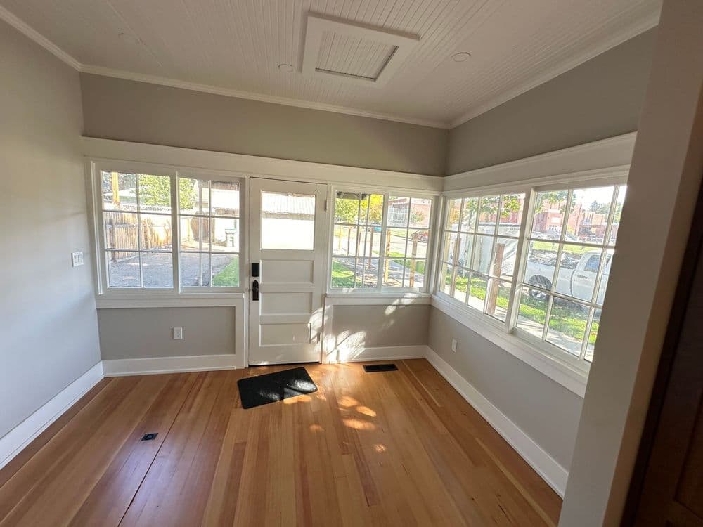 Bright interior view of a home entryway with large windows and wooden floor.