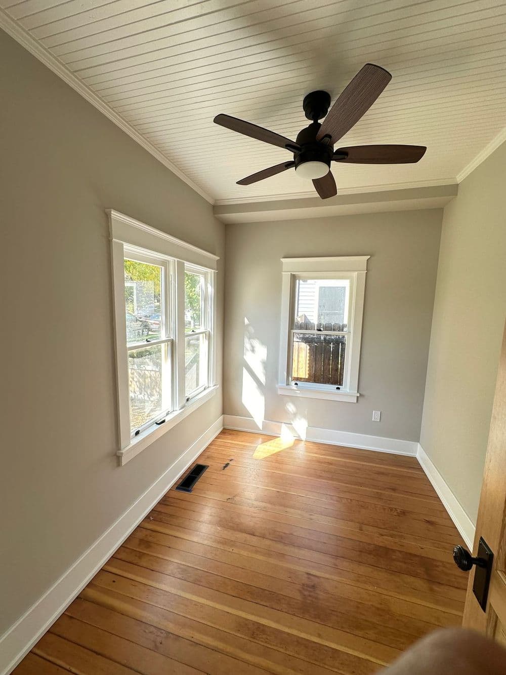 Cozy room with wooden floors, ceiling fan, and sunlight streaming through windows.