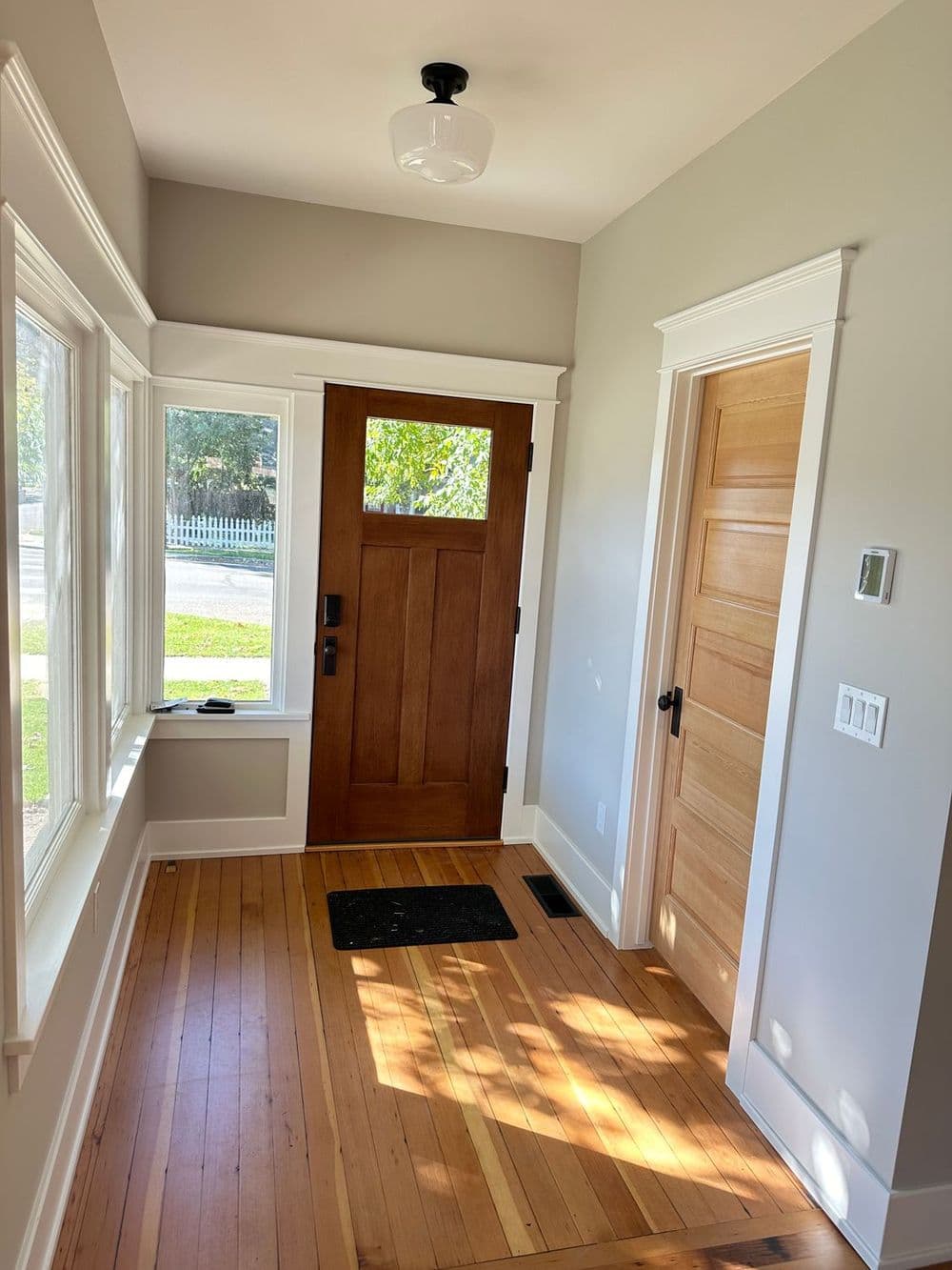 Bright entryway with hardwood floor, large windows, and a wooden front door.