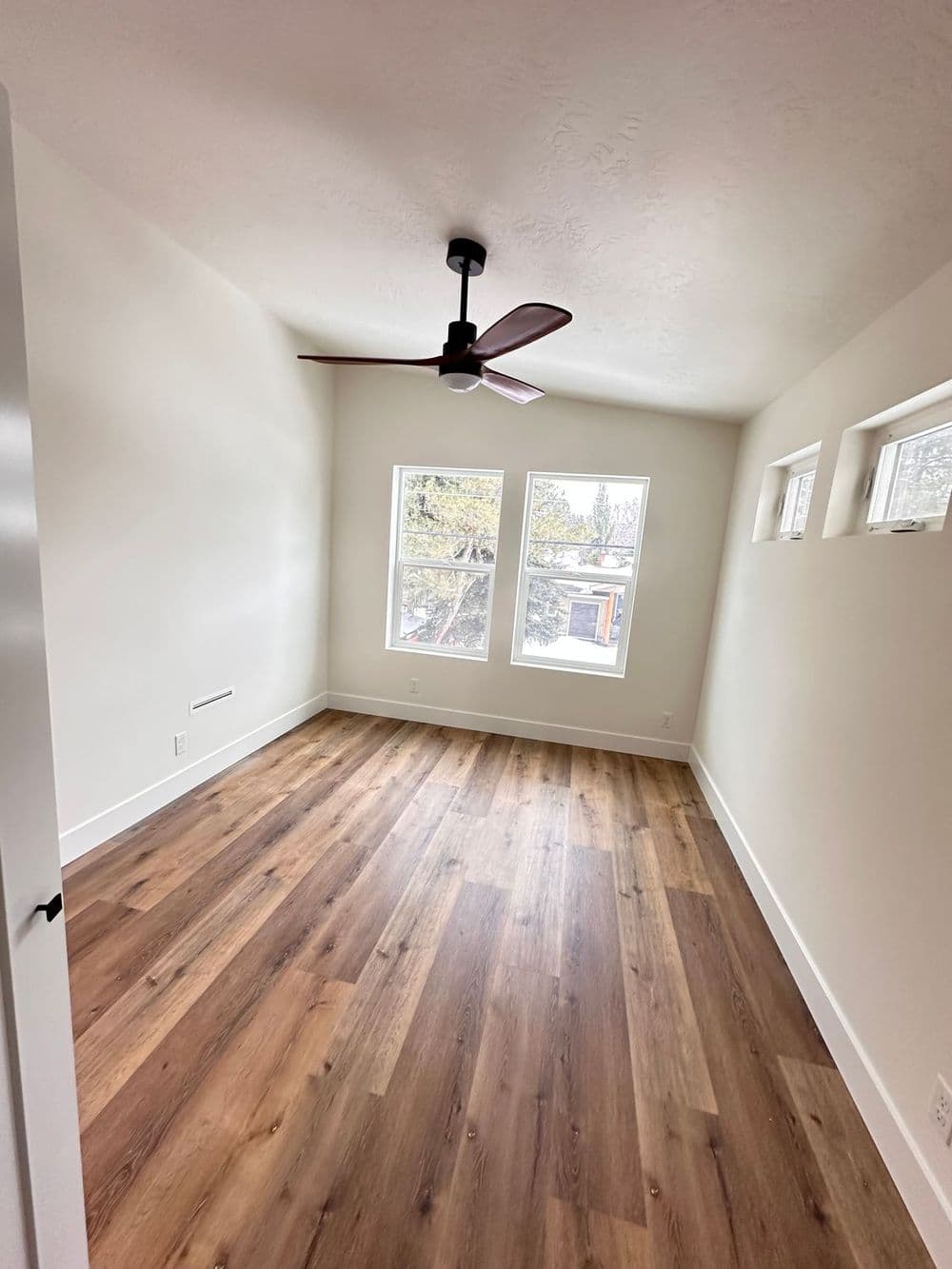 Bright empty room with large windows, wooden floor, and ceiling fan. Ideal for decoration.