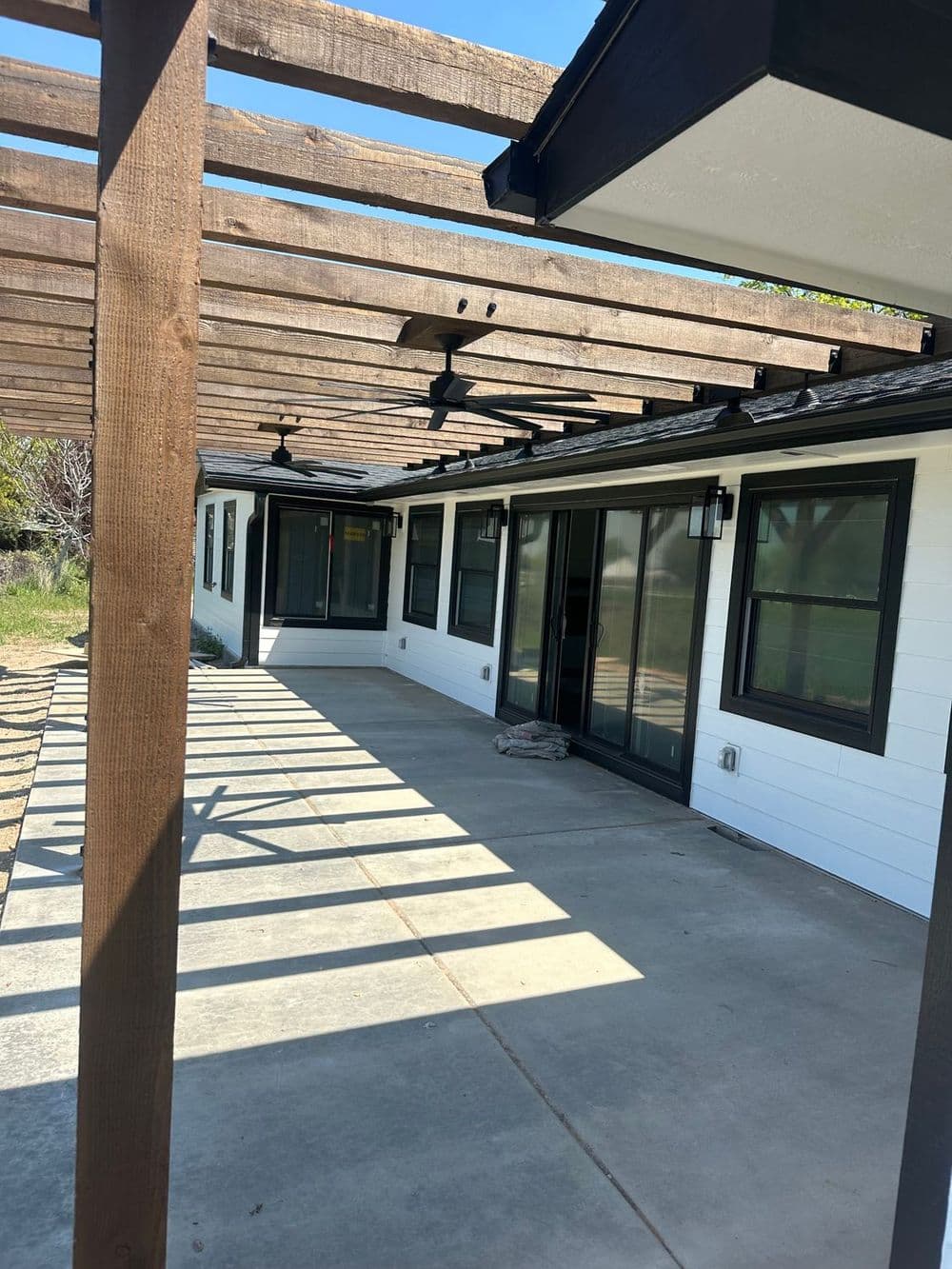Modern home exterior with pergola, concrete patio, and large sliding glass doors.