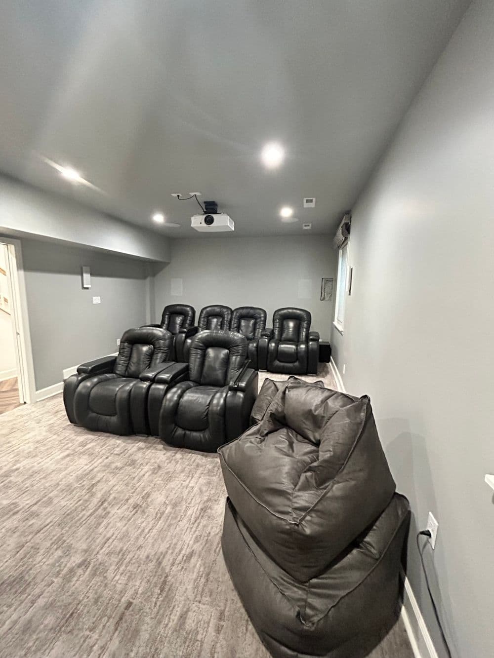 Home theater room with row of black recliners and bean bags on plush carpet.