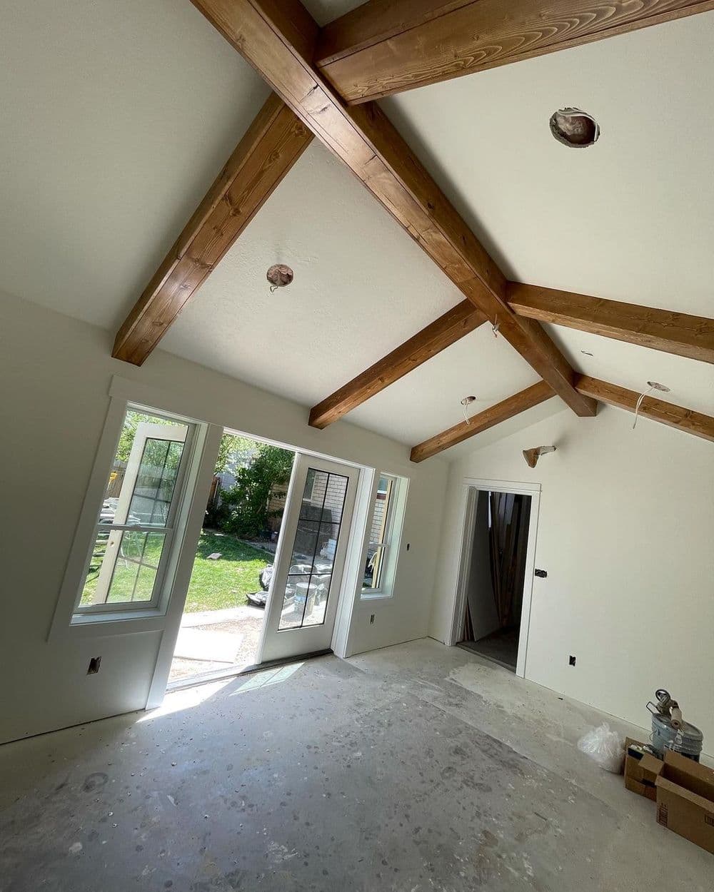 Interior view of a room with exposed wooden beams, large windows, and unfinished flooring.