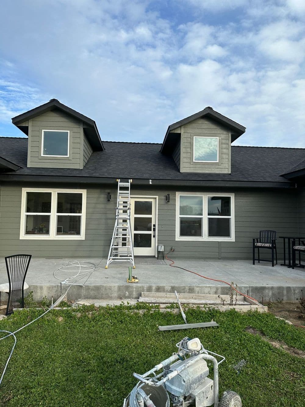 Exterior of a freshly painted gray house with a ladder, chairs, and lawn in foreground.