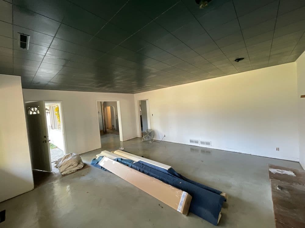 Open living room with bare concrete floor, unfinished walls, and construction materials scattered.