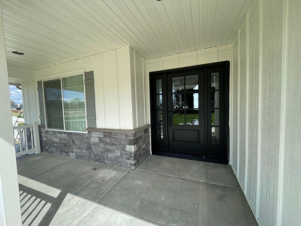 Modern front porch with black double doors, stone accents, and large window.
