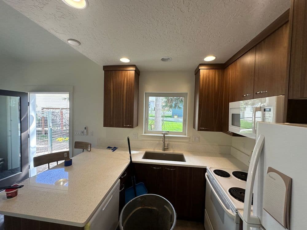 Modern kitchen with wooden cabinets, white countertops, and appliances including a stove and sink.