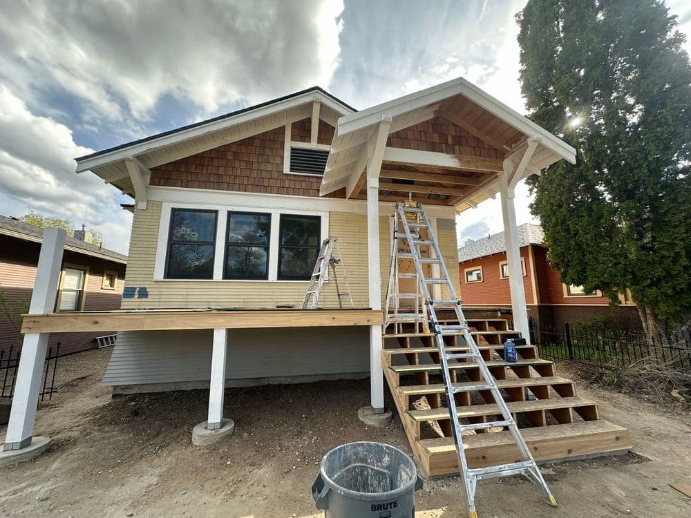 Home renovation in progress with ladders, wooden steps, and a cloudy sky.