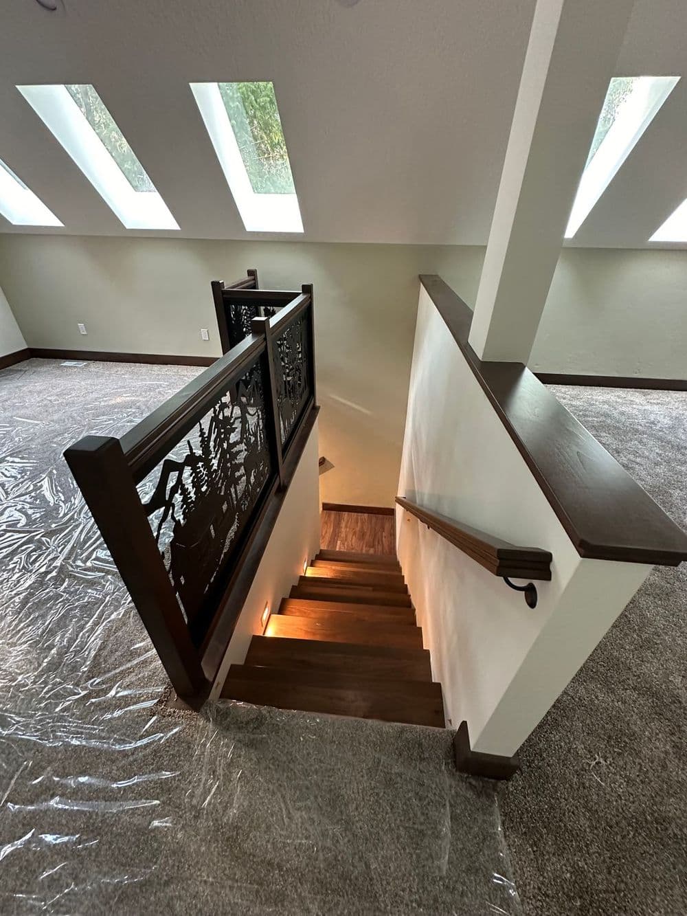 Wooden staircase with decorative railing and skylights, leading to a carpeted lower level.