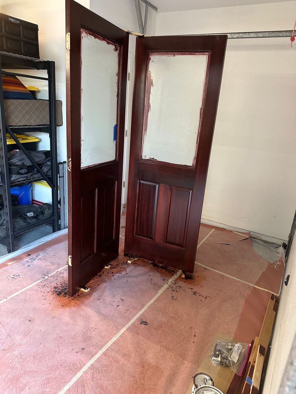 Two wooden doors with fresh dark stain, propped open in a garage with protective covering on the floor.