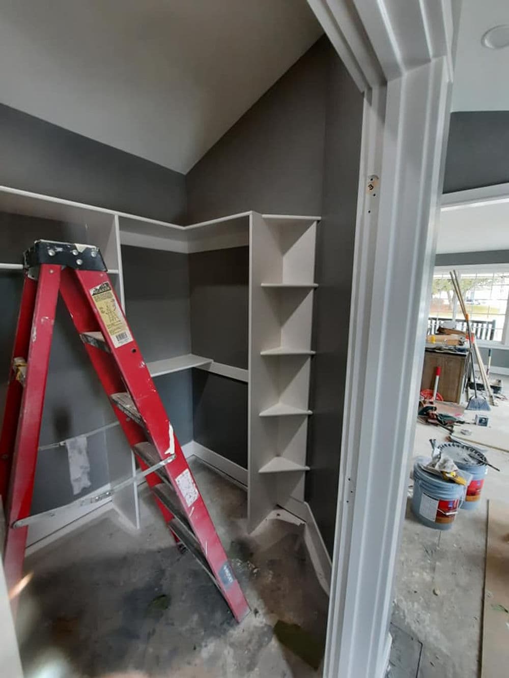 Red ladder in a room with gray walls and white shelving during renovation.