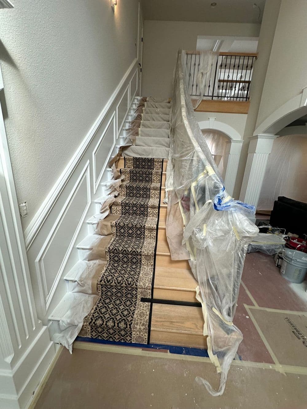 Wooden staircase under renovation, covered with plastic, featuring a decorative runner.