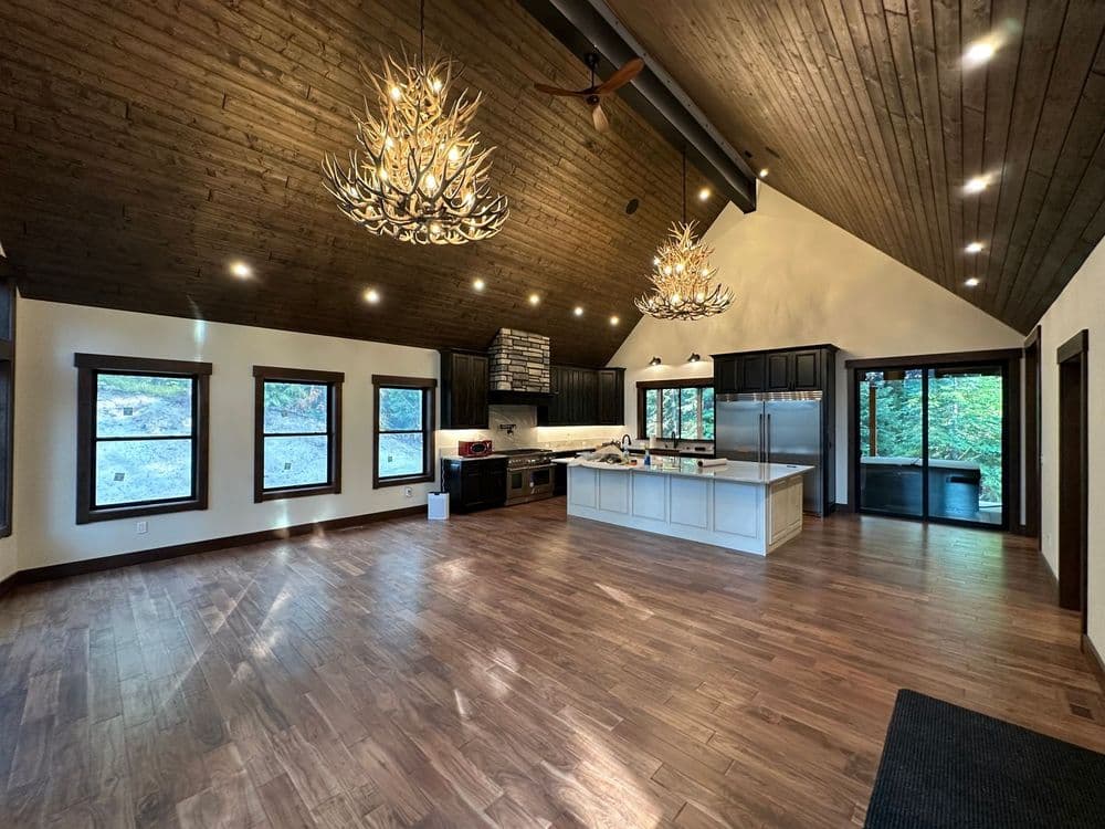 Modern kitchen with wooden ceiling, large island, and bright windows overlooking nature.