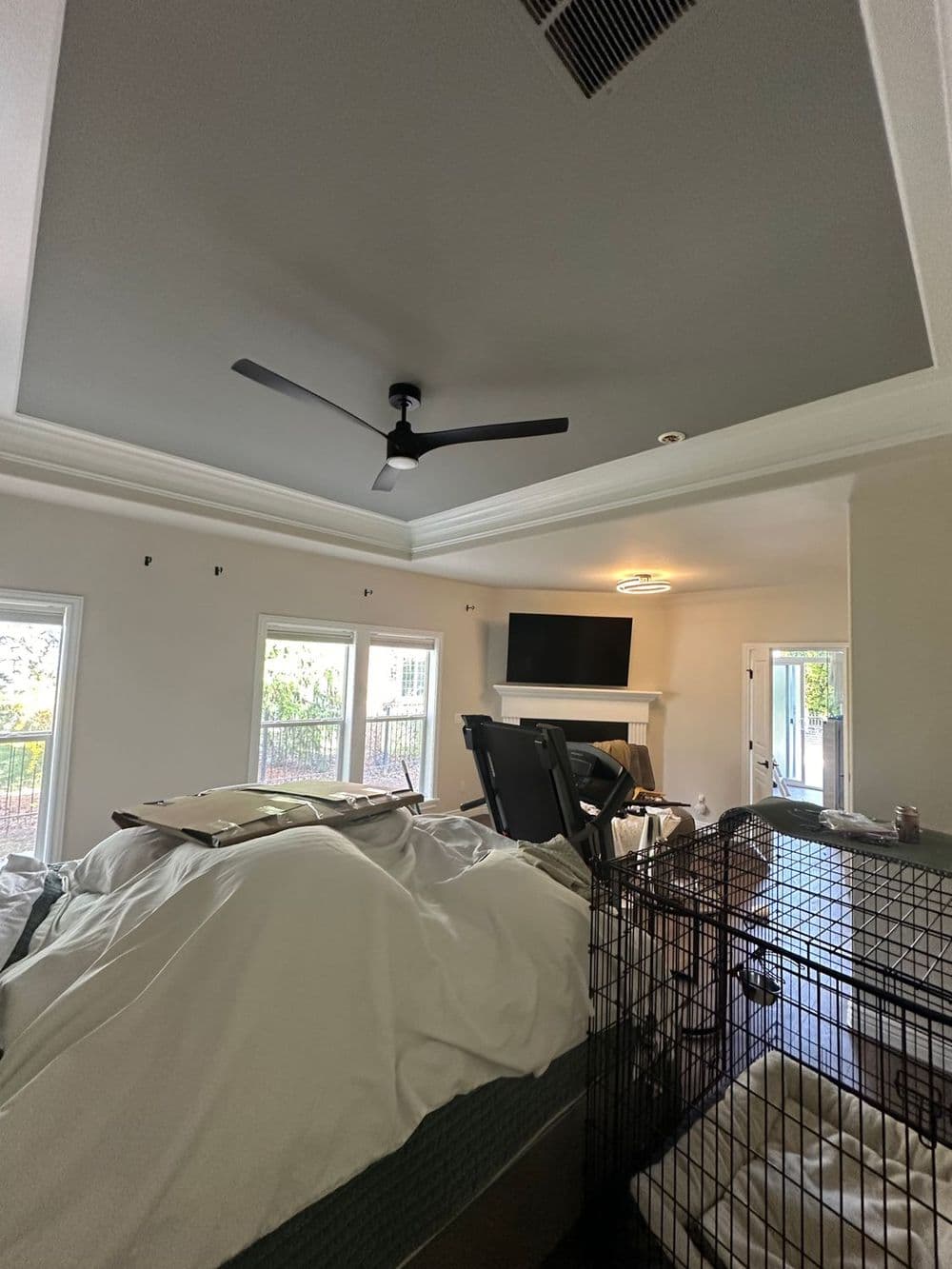 Modern bedroom with a ceiling fan, television, and natural light from large windows.