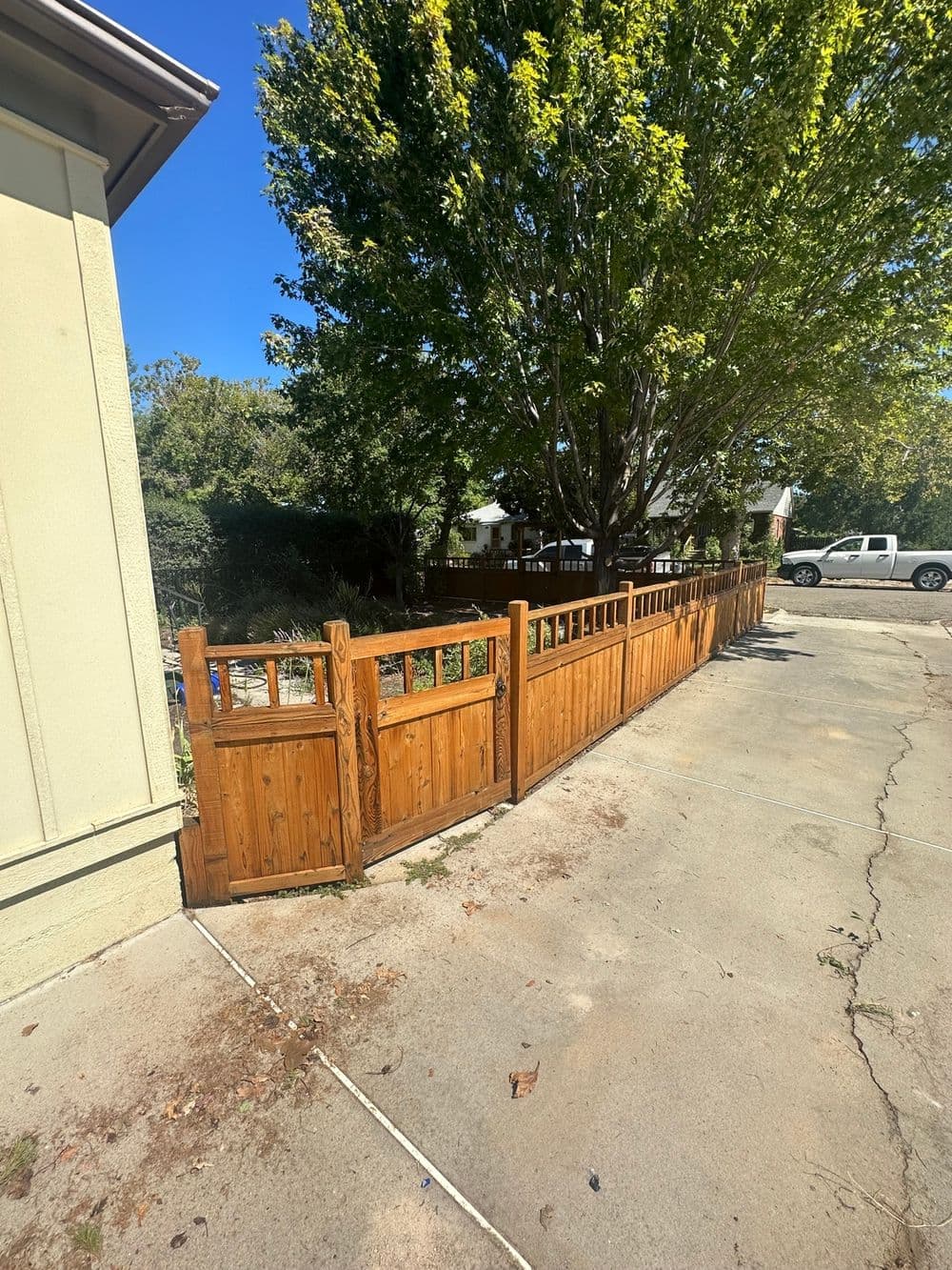 Wooden fence along pavement with a tree in the background and a parked white truck.