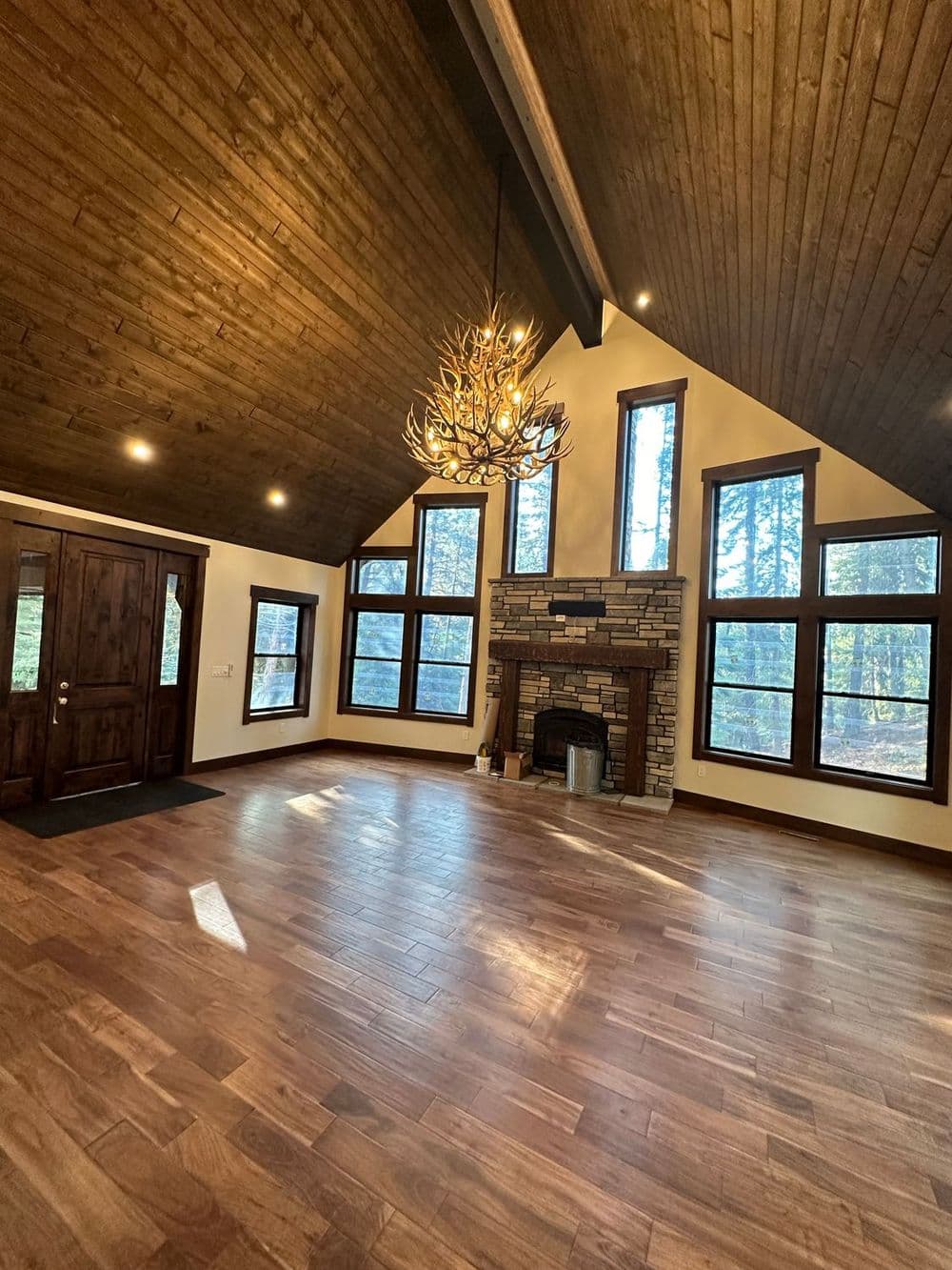 Spacious living room with vaulted wooden ceiling, stone fireplace, and large windows.