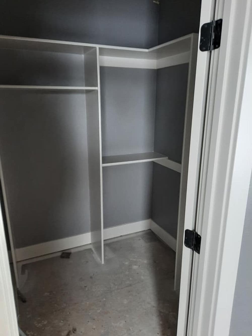 Empty closet with white shelves and gray walls, featuring a door partially open.