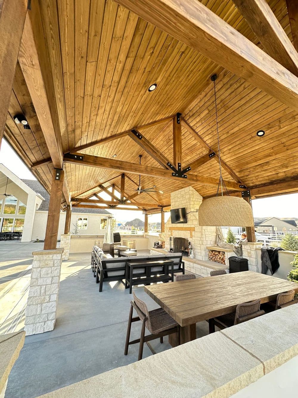 Spacious outdoor patio with wooden beams, fireplace, and dining area in a modern design.