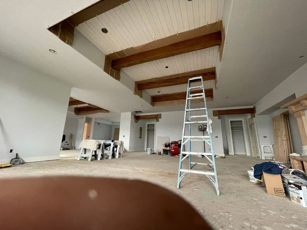 Interior renovation showcasing wooden beams, a ladder, and construction materials in a spacious room.