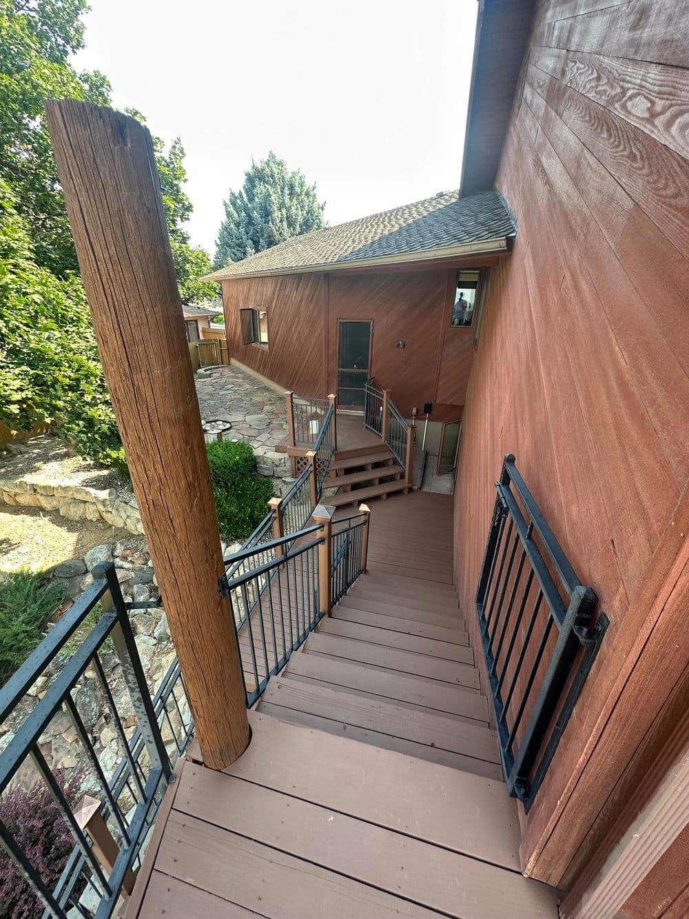 Wooden staircase leading down to landscaped patio from modern home exterior.