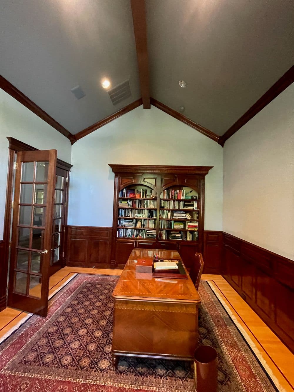 Elegant wooden office with a large desk, bookshelves, and a warm carpeted floor.