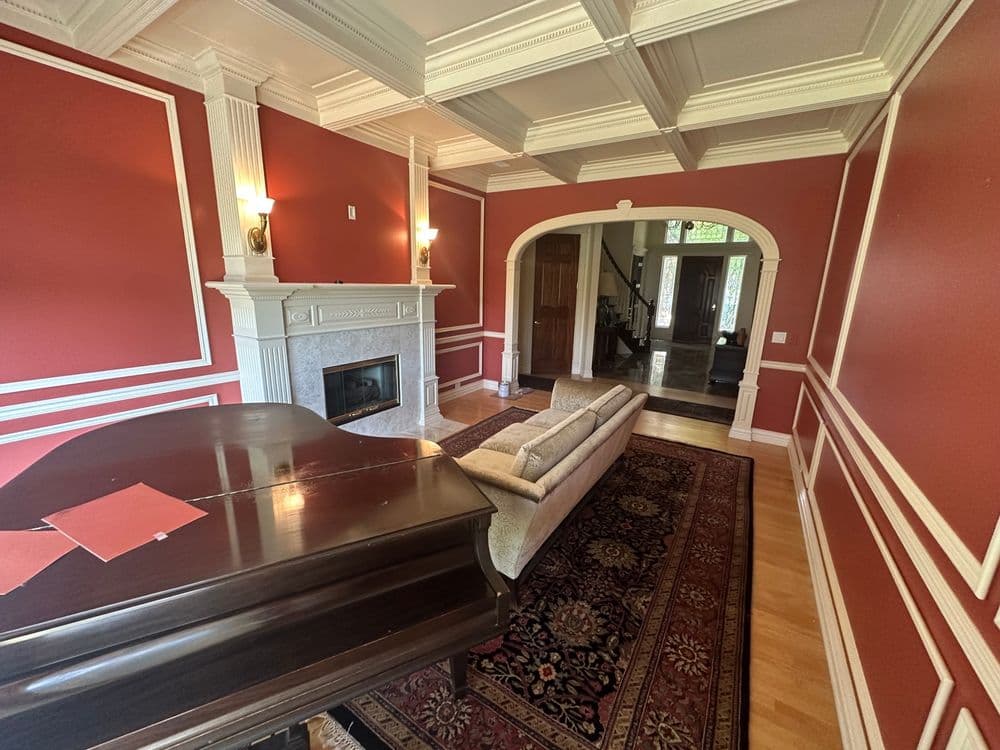 Elegant living room with red walls, a grand piano, and a cozy seating area near a fireplace.
