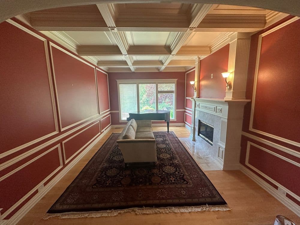 Living room with red walls, coffered ceiling, fireplace, and large area rug.