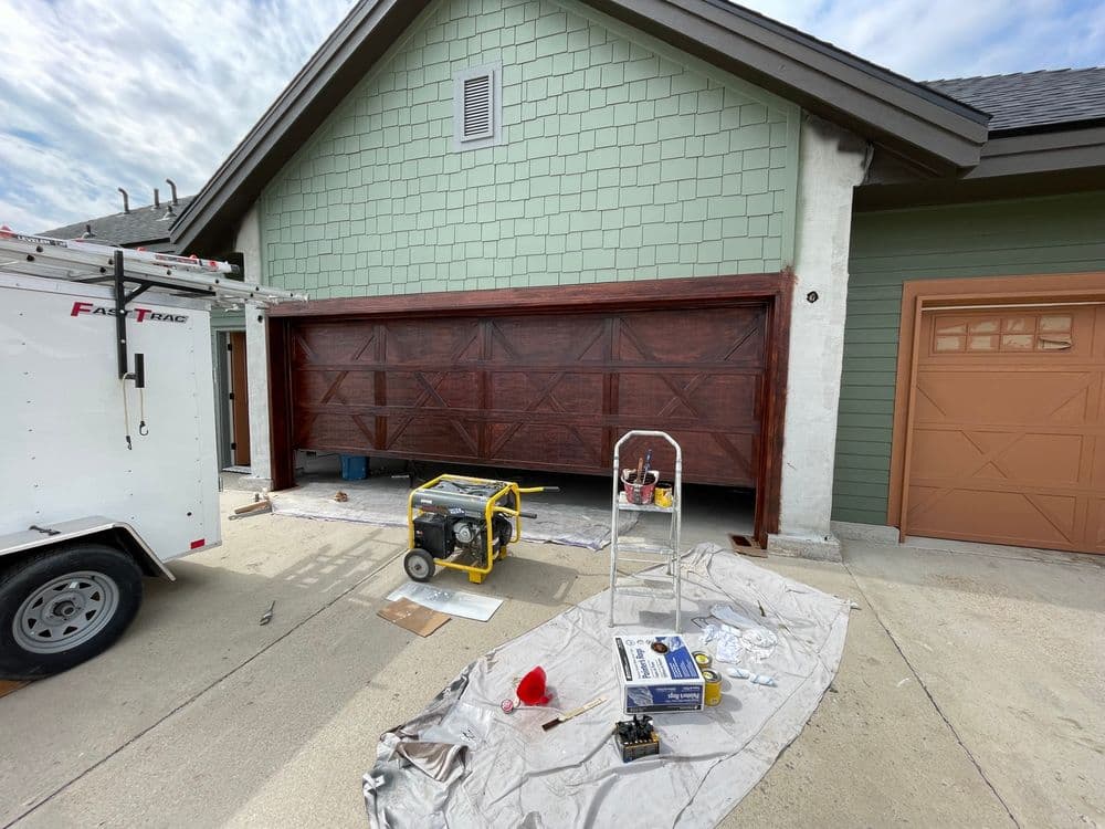 Garage door installation with tools and equipment outside a house under a cloudy sky.
