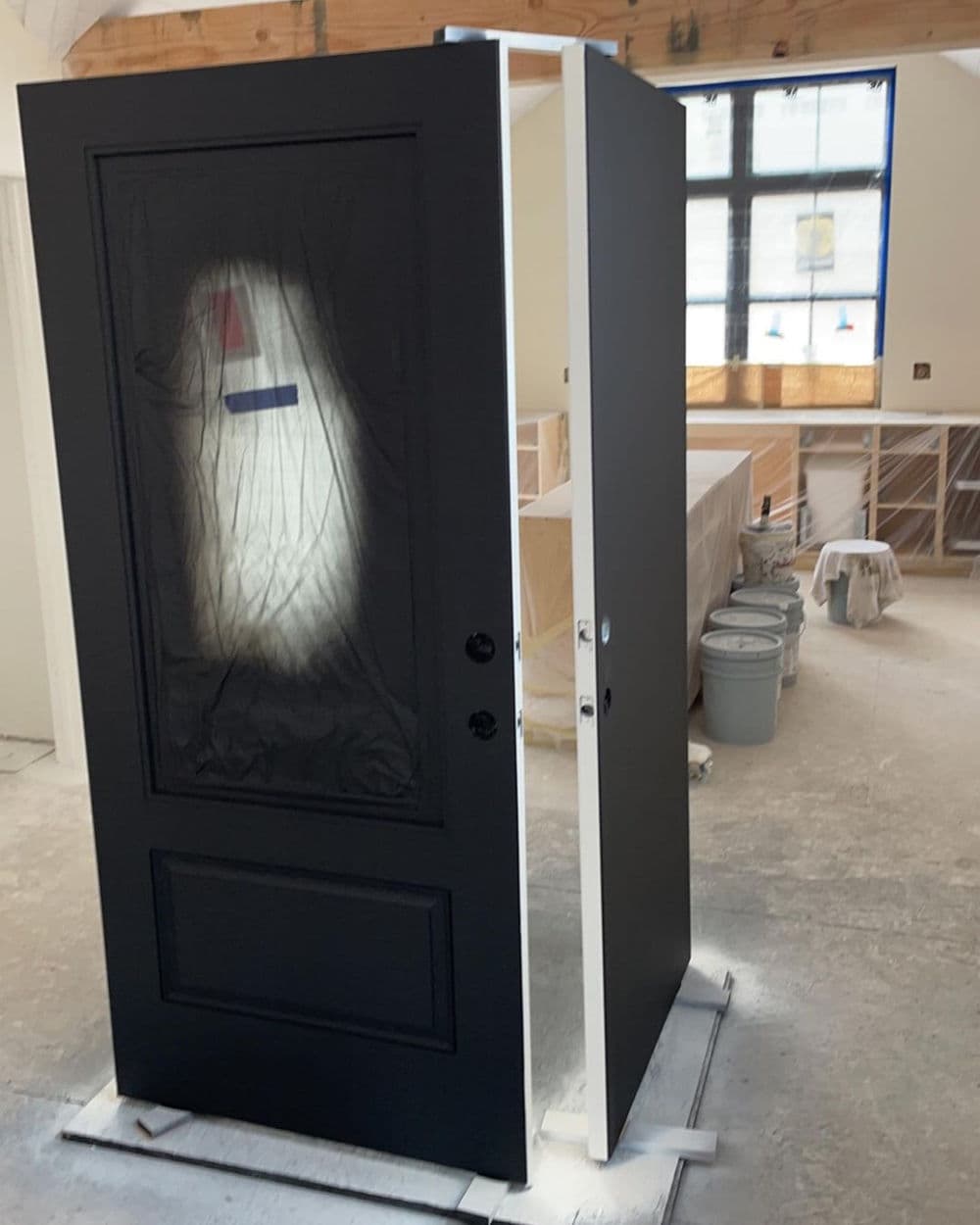 Black front door with a window, partially installed in a home under construction.
