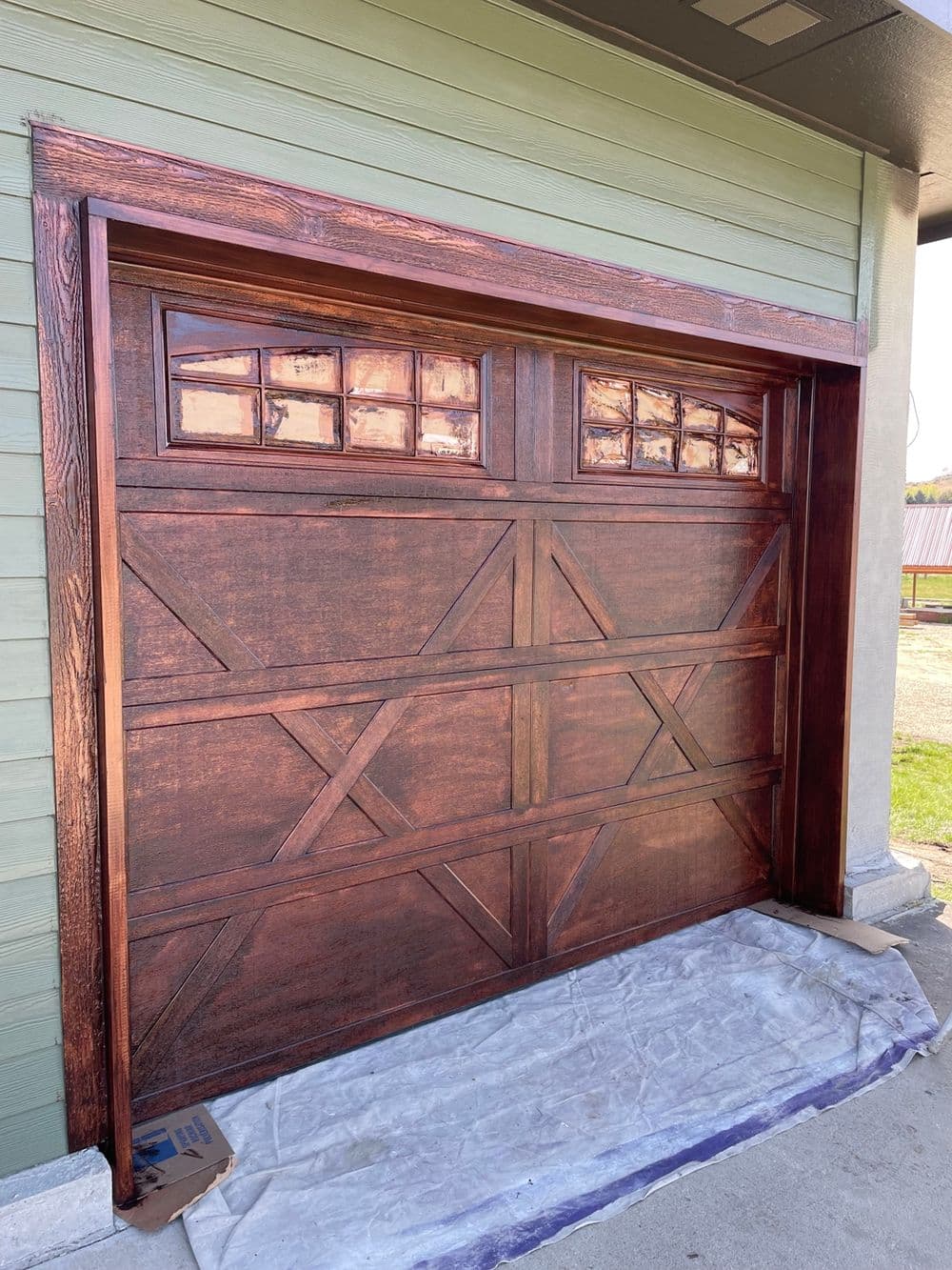 Wooden garage door with decorative windows, framed in rich brown tones, set against a green wall.