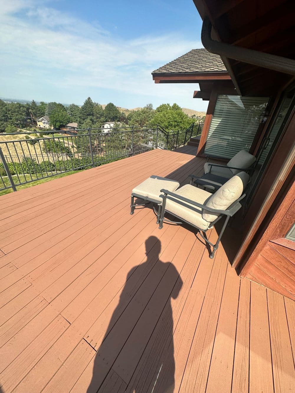 Sunlit wooden deck with lounge chairs and a scenic view of trees and hills.