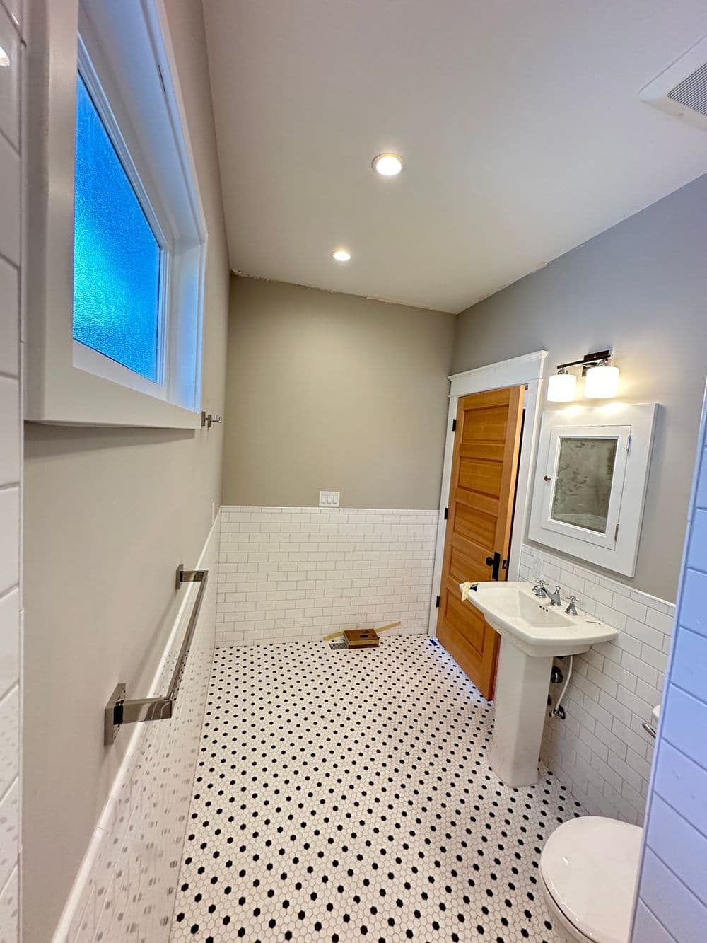 Modern bathroom featuring white subway tiles, black and white hexagon floor, and wooden door.