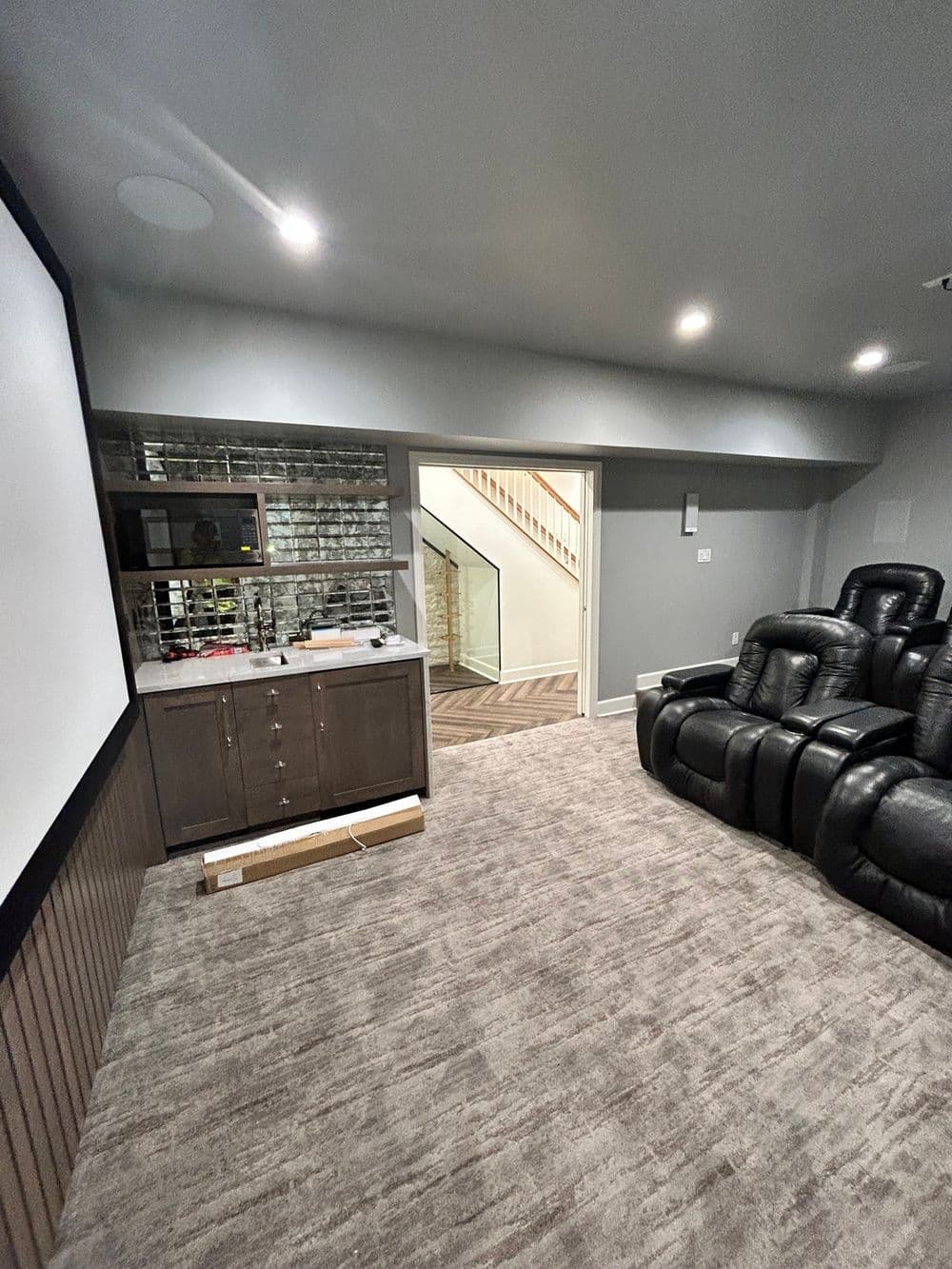 Home theater room with black recliner chairs, wet bar, and staircase in a modern design.