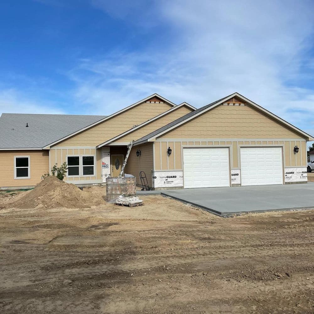 Newly built single-story home with beige exterior, double garage, and surrounding construction site.