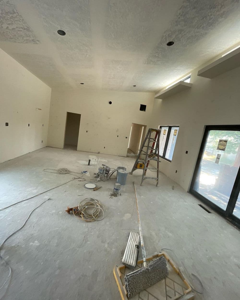 Interior of a partially renovated room with a ladder, paint supplies, and unfinished walls.