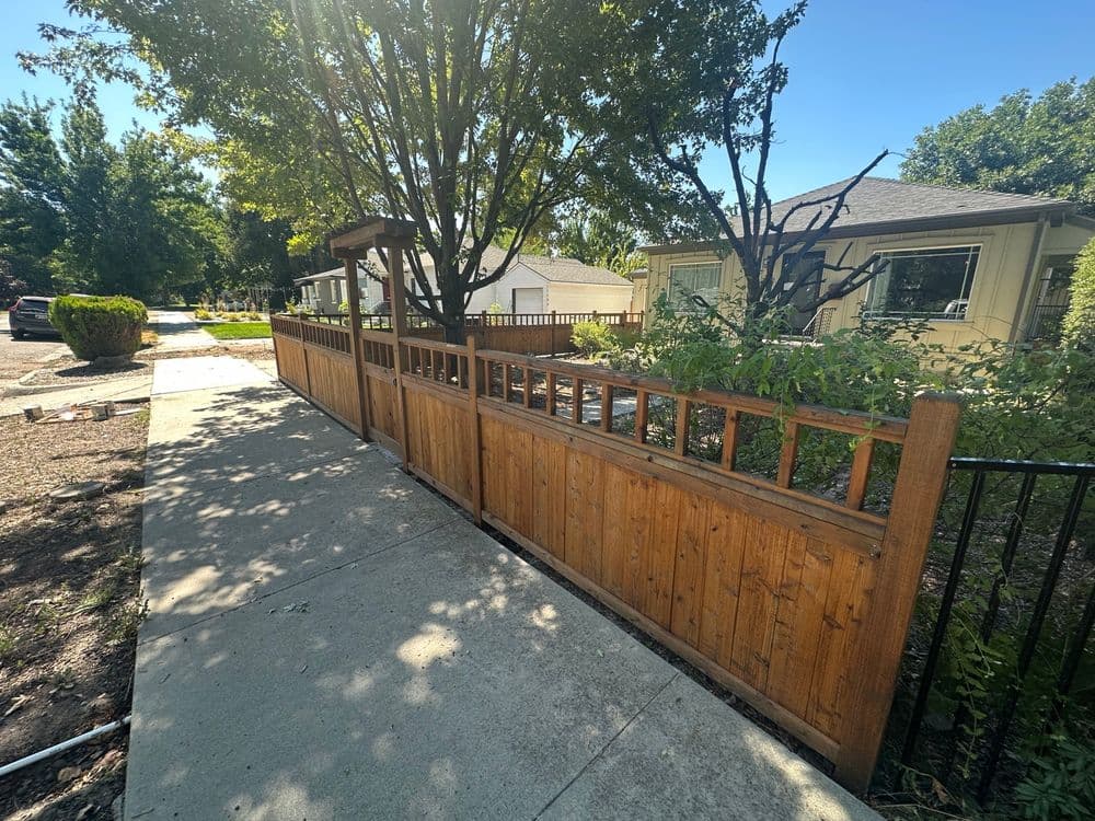 Wooden fence alongside a walkway with trees and residential homes in the background.