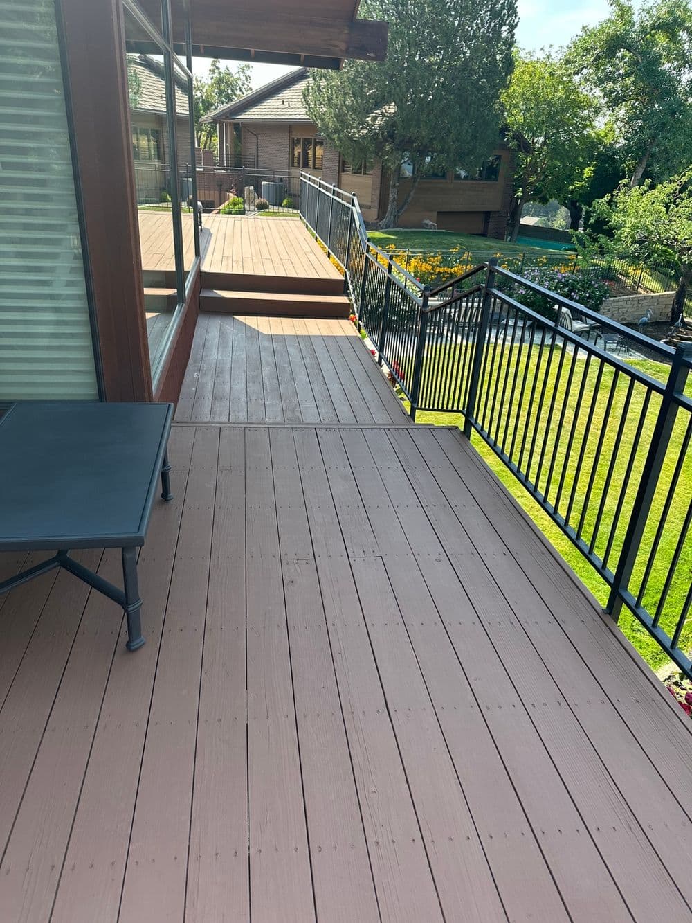 Deck view with wooden flooring, railing, and surrounding landscaped yard in sunlight.
