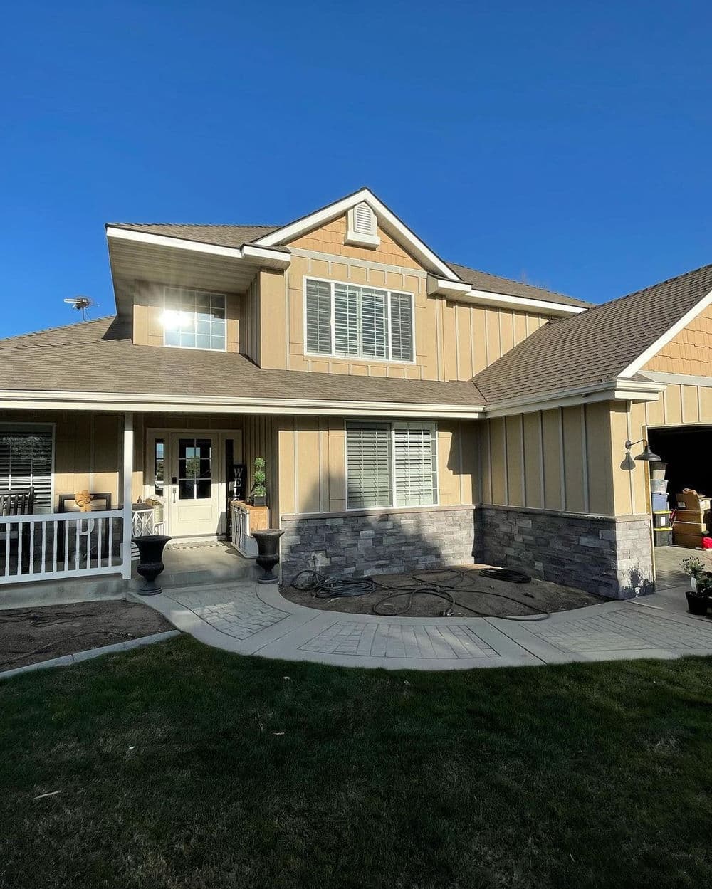 Two-story house with beige siding, stone accents, and a landscaped front yard under a blue sky.