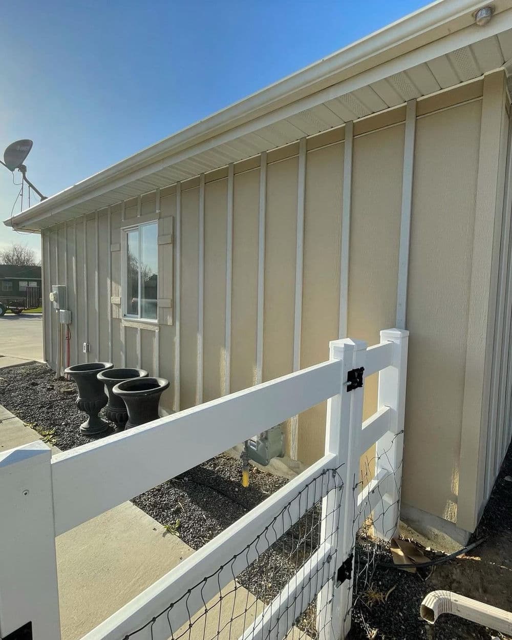 Side view of a beige building with satellite dish and decorative pots near a white fence.