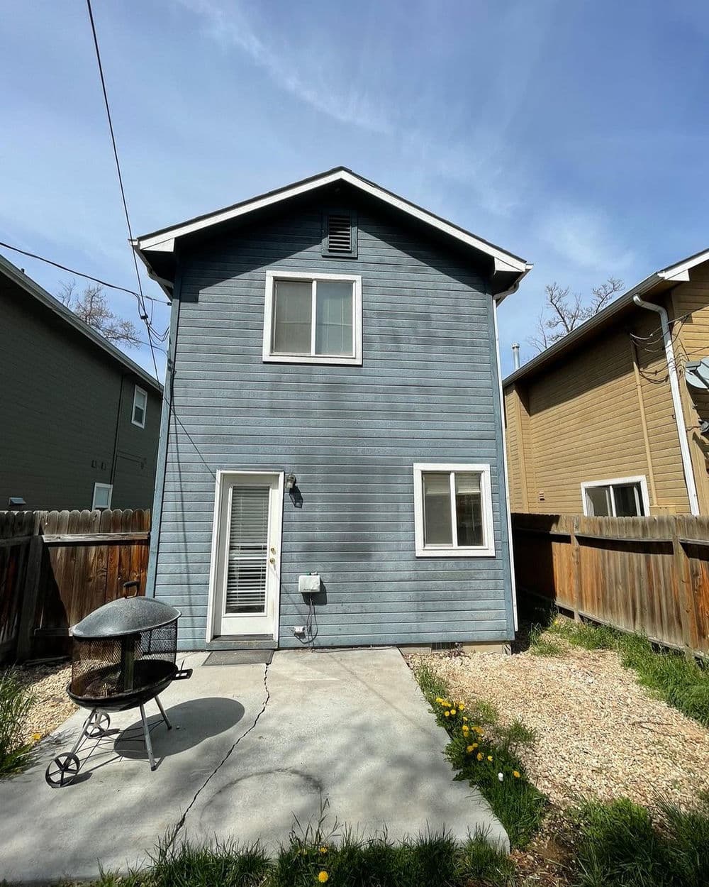 Two-story blue house with backyard, concrete patio, and fire pit on a sunny day.